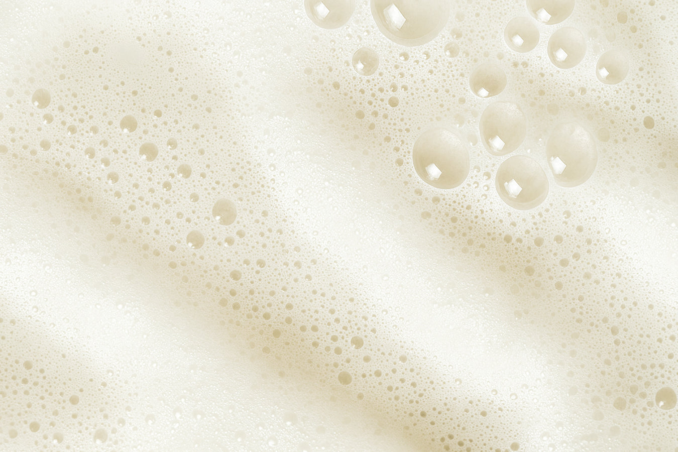 A close-up view of soft beige foam with tiny and large bubbles. The image captures a light, airy texture that evokes cleanliness and freshness.