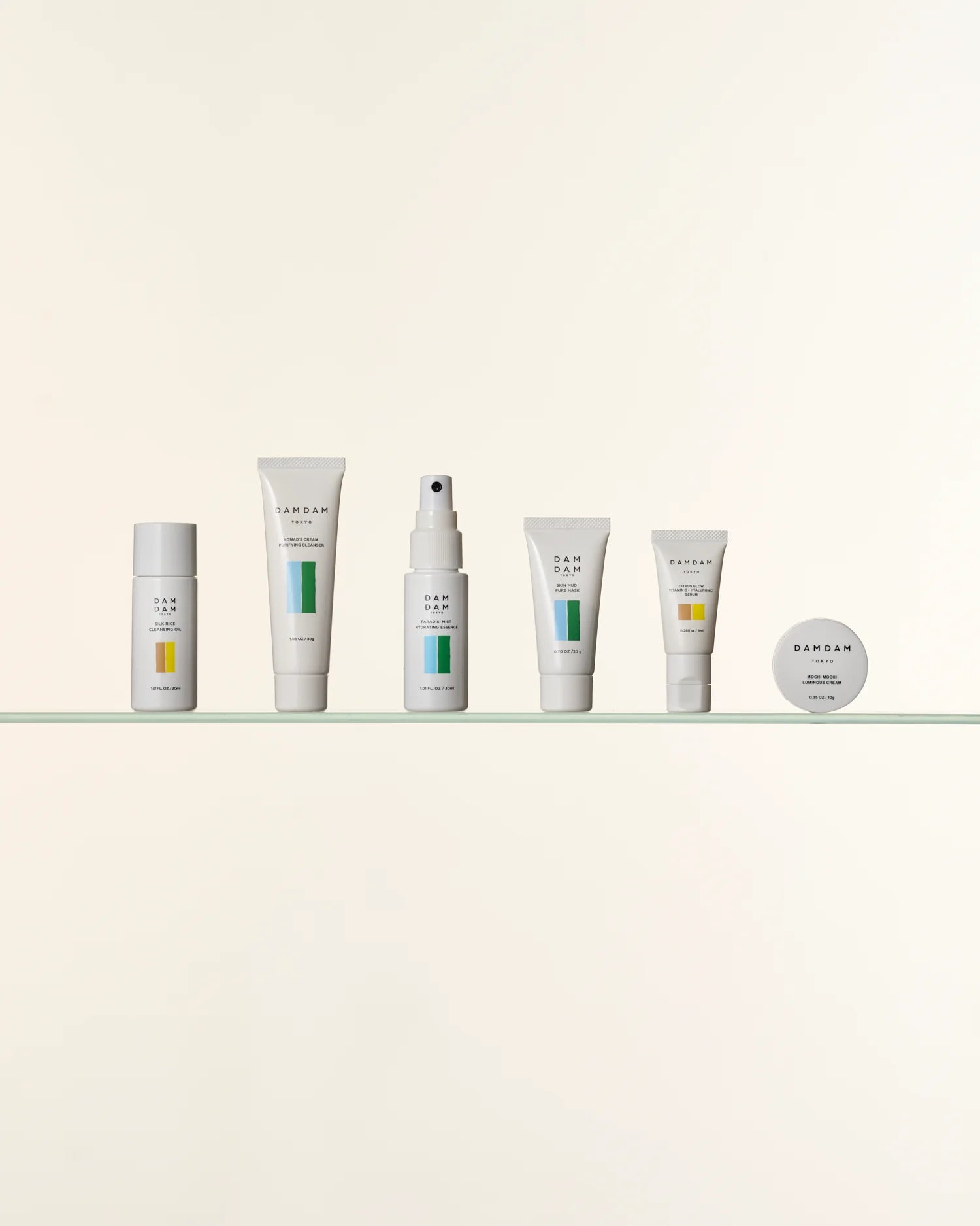 A minimal arrangement of DAMDAM skincare products lined up neatly on a glass shelf against a soft beige background. The clean design and balanced colors emphasize simplicity and modern Japanese aesthetics.