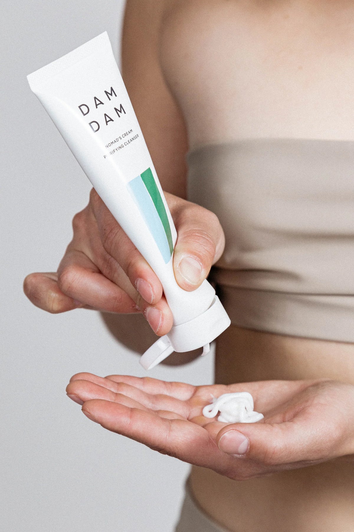 A person squeezes DAMDAM Nomad’s Cream Purifying Cleanser from a white tube into their hand. The close-up focuses on the creamy texture and simple, elegant product design.