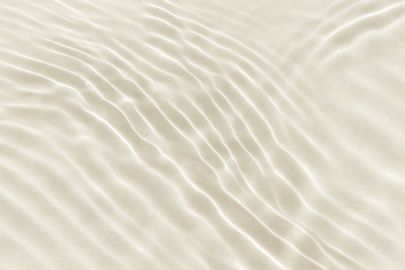A close-up of fine sand with gentle ripples illuminated by soft light. The smooth, flowing lines create a calming and organic texture.