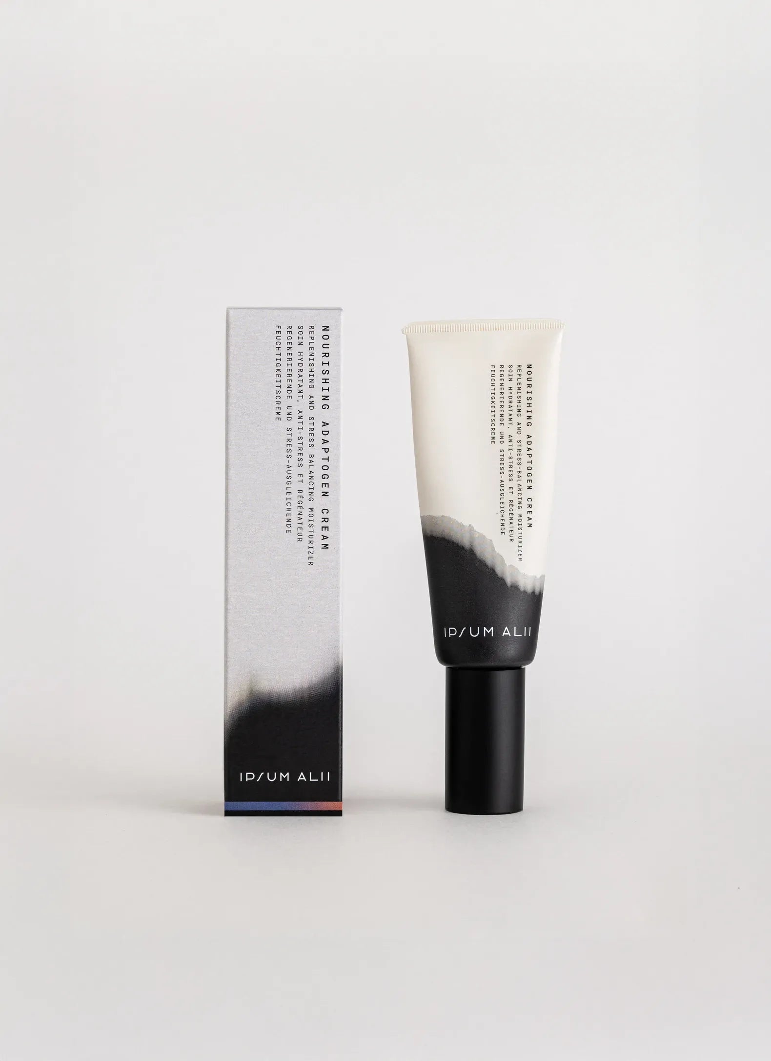 A tube of Ipsum Ali Nourishing Adaptogen Cream standing next to its box against a plain light background. Both the tube and box feature a minimalist black-and-white gradient design with vertical text.