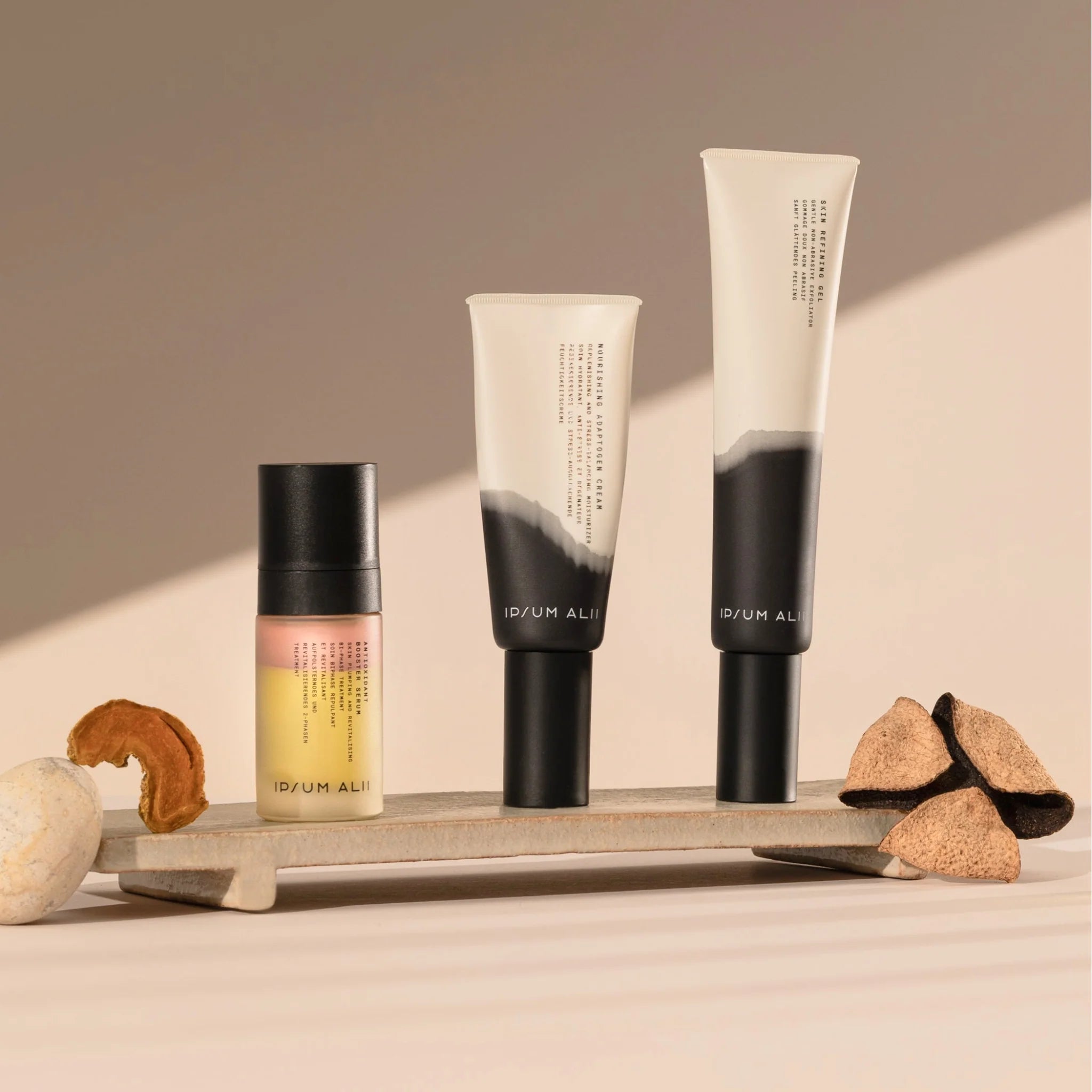 Ipsum Alii skincare trio — a serum and two refining creams — displayed on a beige surface with natural elements under warm, soft light, emphasizing the brand’s minimalist and organic aesthetic.