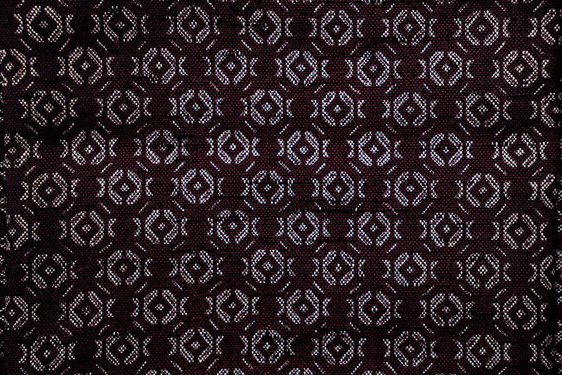 A piece of kimono fabric featuring an intricate, woven geometric pattern in varying shades of Burgundy.