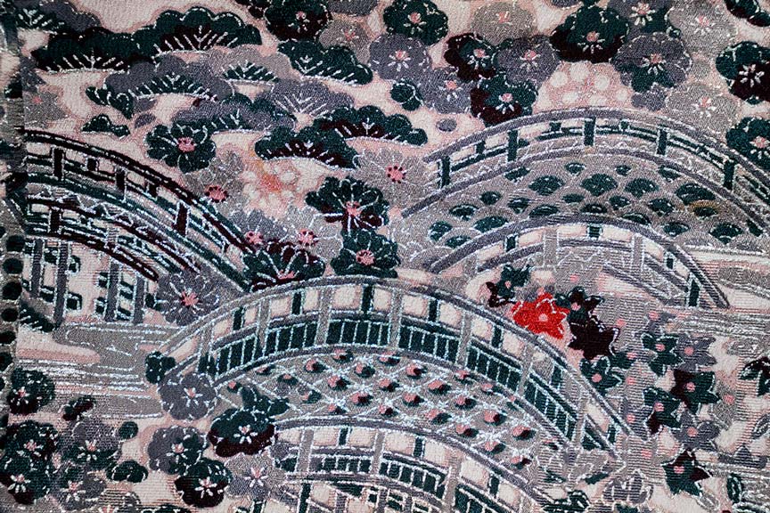 A piece of kimono fabric featuring an intricate, woven pattern in varying shades of purple, soft pink and deep blue/green.