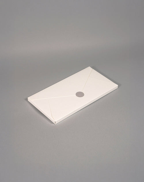 A sleek, minimalist white envelope-style package rests on a neutral grey background, sealed with a simple round sticker. The design evokes elegance and simplicity, ideal for premium or eco-conscious branding.