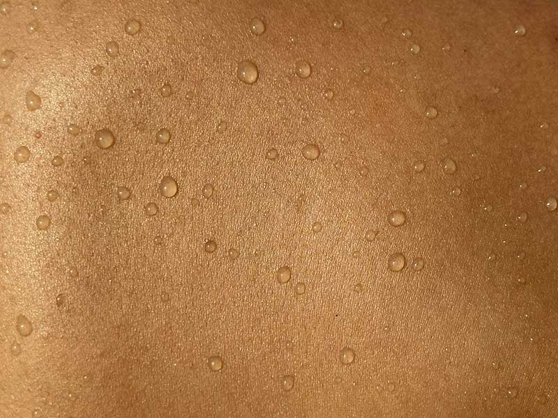 Close-up of dewy, hydrated skin with water droplets on a warm golden-brown surface, highlighting moisture and glow.