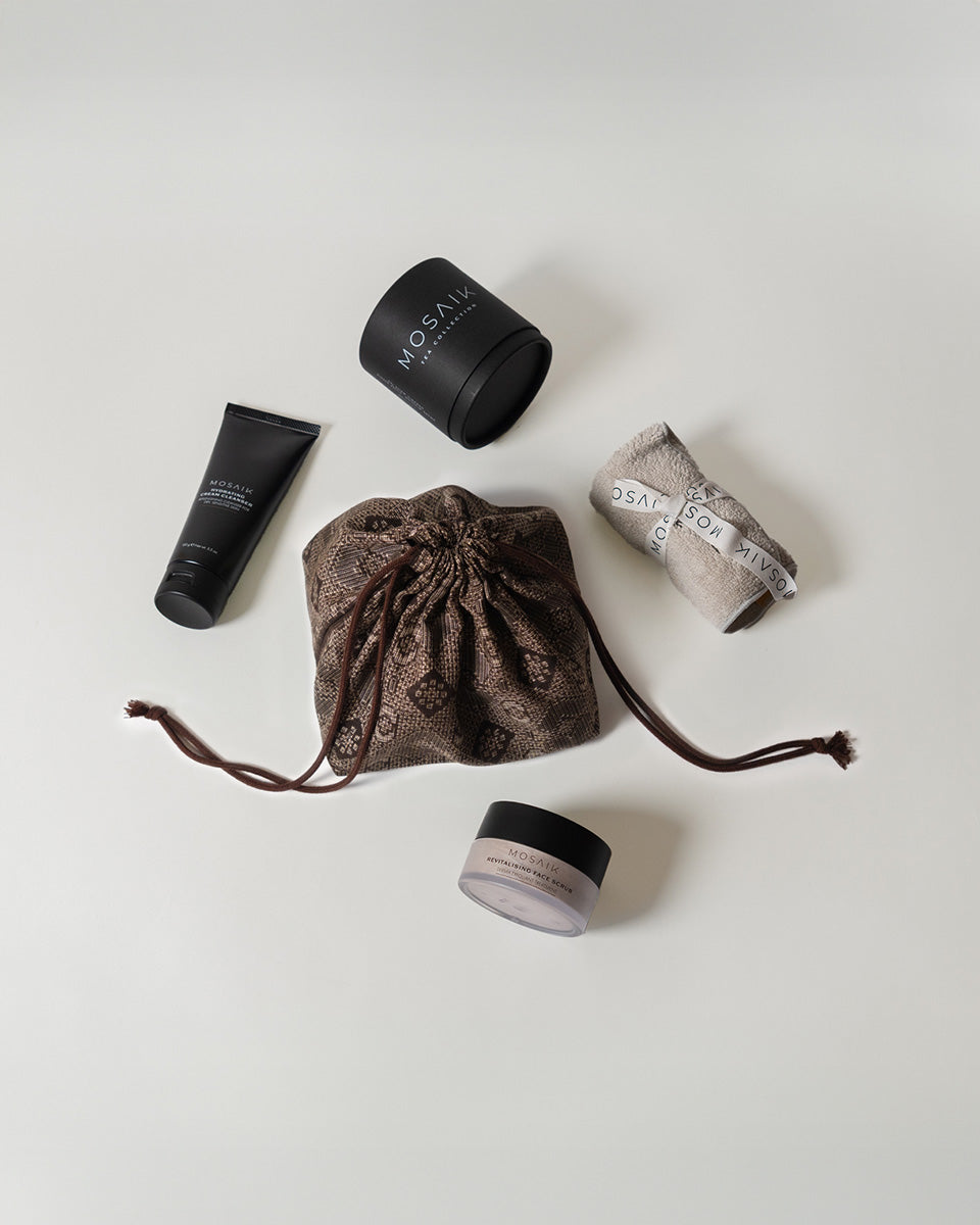 A stylish flat lay of Mosaik skincare products and a patterned drawstring bag arranged on a light surface.