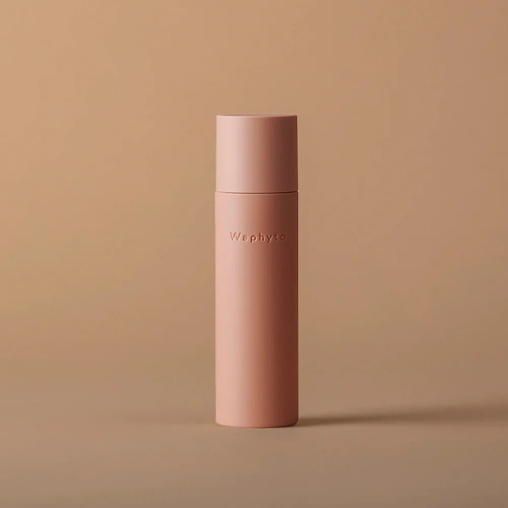 A tall, peach-colored bottle labeled “Waphyto” stands on a beige surface with a matching background. The minimalist design and warm tones create a calm, elegant aesthetic.