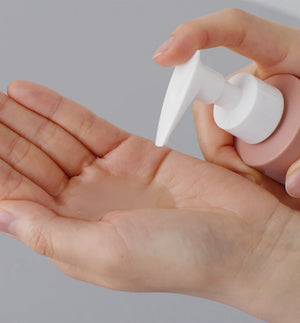 A person pumps a small amount of skincare product from a bottle into their hand. The image highlights the texture and gentle application of the formula.
