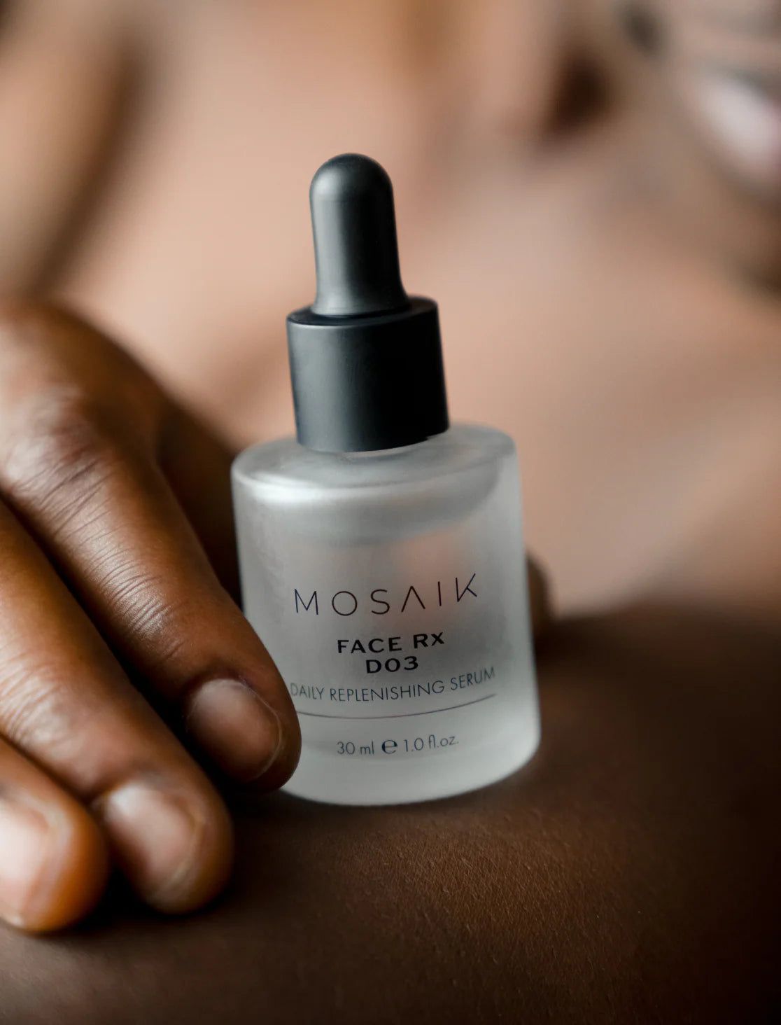 Close-up of a person’s hand holding a frosted glass bottle of MOSAIK Face Rx D03 Daily Replenishing Serum, highlighting the product’s sleek minimalist design against natural skin tones.