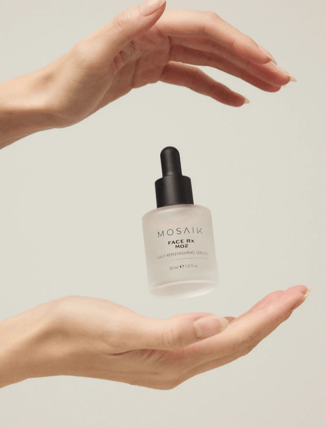 Close-up of two hands gently framing a floating bottle of MOSAIK Face Rx MO2 Daily Replenishing Serum against a soft neutral background, emphasizing balance and minimalism.