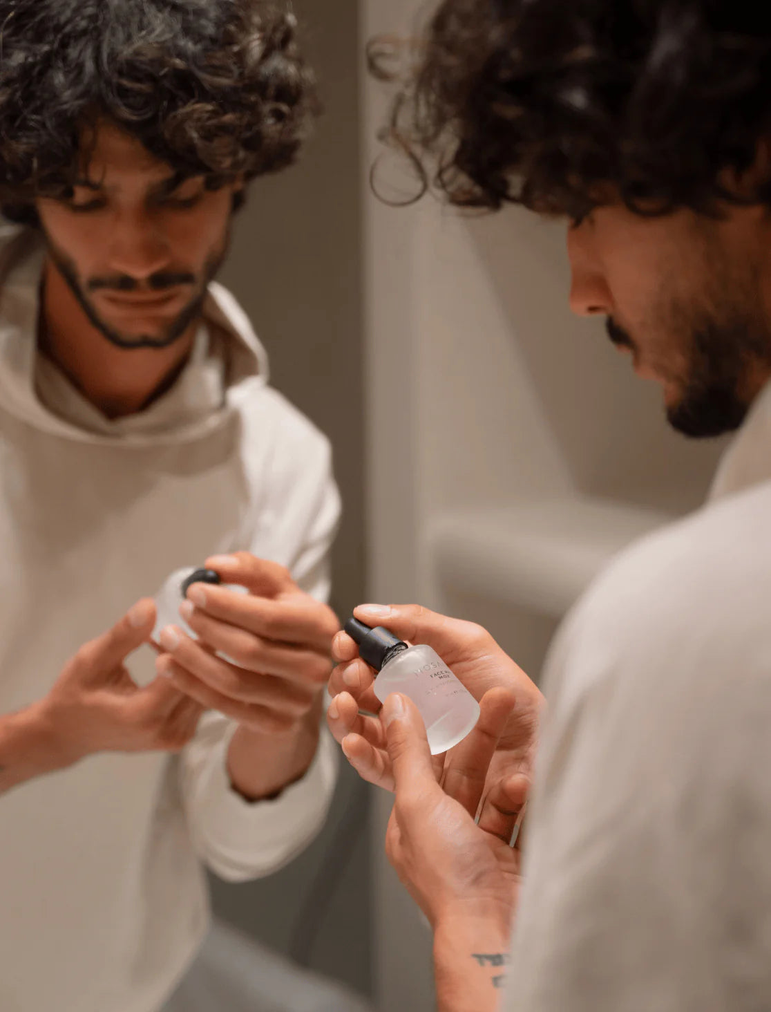 Close-up of two hands gently framing a floating bottle of MOSAIK Face Rx MO2 Daily Replenishing Serum against a soft neutral background, emphasizing balance and minimalism.