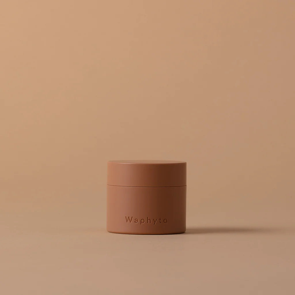 A small peach-colored Waphyto jar sits on a beige surface against a matching background. The minimalist composition emphasizes simplicity and natural elegance.