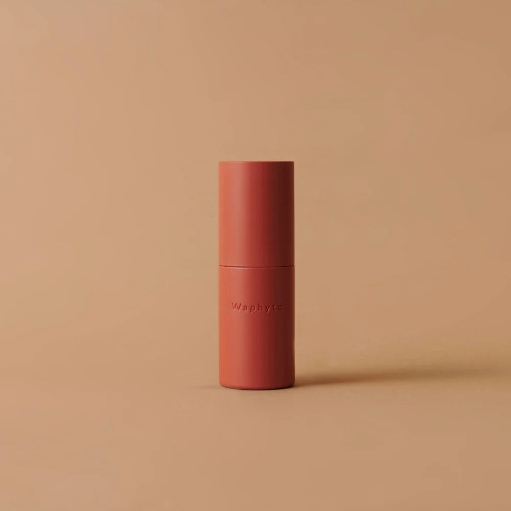 A coral-colored Waphyto bottle stands upright on a soft beige surface. The simple background and design emphasize elegance and modern minimalism.